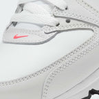 Close-up of a white leather Nike shoe showing the side panel, white laces, contrast stitching, and a small pink Nike swoosh logo.