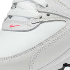 Close-up of a white leather Nike shoe showing the side panel, white laces, contrast stitching, and a small pink Nike swoosh logo.