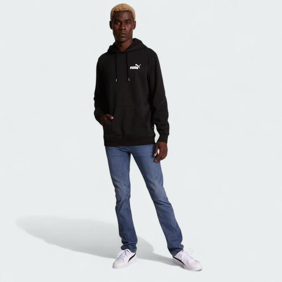 distant model view off the Puma Essential Small Logo Overhead Fleece Hoodie in black, showing the soft fleece fabric texture and the detailed embroidered Puma Cat Logo.