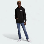 distant model view off the Puma Essential Small Logo Overhead Fleece Hoodie in black, showing the soft fleece fabric texture and the detailed embroidered Puma Cat Logo.