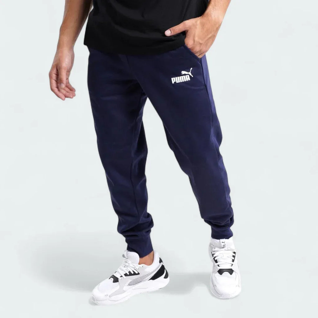 Puma Essential Logo Pants Men's in navy fleece, front view worn by a model showing the elastic waistband, drawcord, and a white Puma Cat Logo on the thigh.