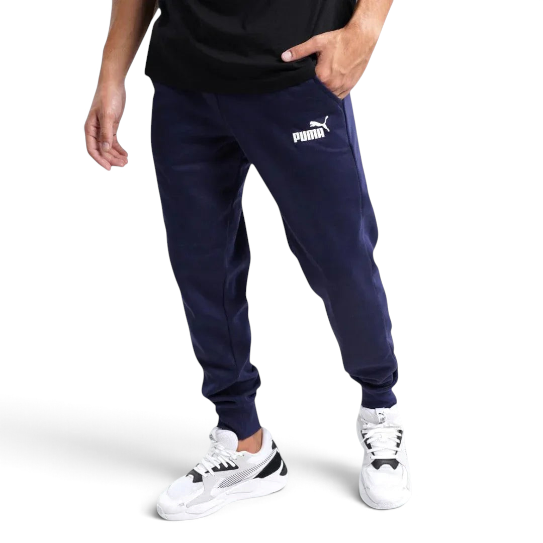 Puma Essential Logo Pants Men's in navy fleece, front view worn by a model showing the elastic waistband, drawcord, and a white Puma Cat Logo on the thigh. Main image