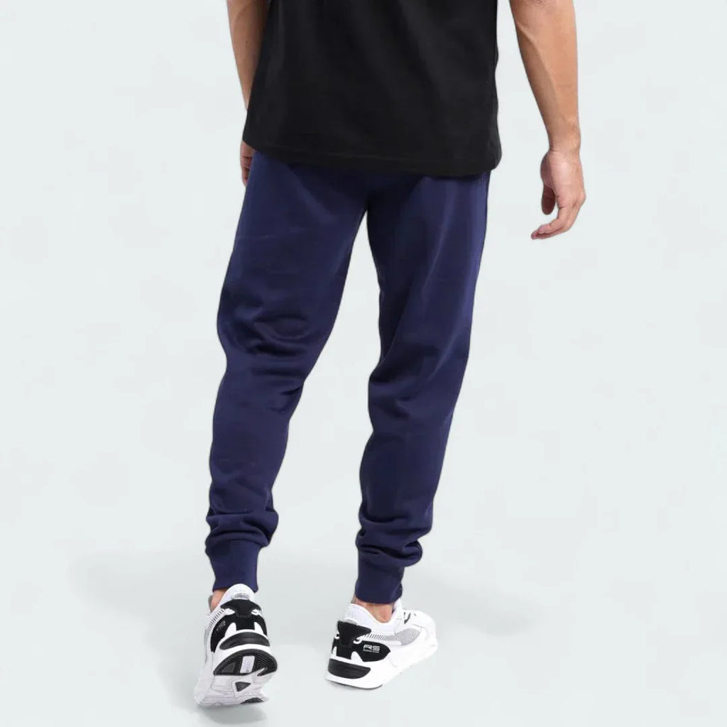 Puma Essential Logo Pants Men's in navy fleece, back view worn by a model showcasing the tapered leg design and ribbed cuffs.