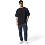 Man wearing a black oversized t-shirt and navy pants with a brand logo on a light gray background