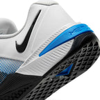 Close-up shot focusing on the rear outsole and heel construction, showing the grooved white foam midsole, black rubber outsole with diamond-pattern tread, black Swoosh, and the blue Metcon heel clip.
