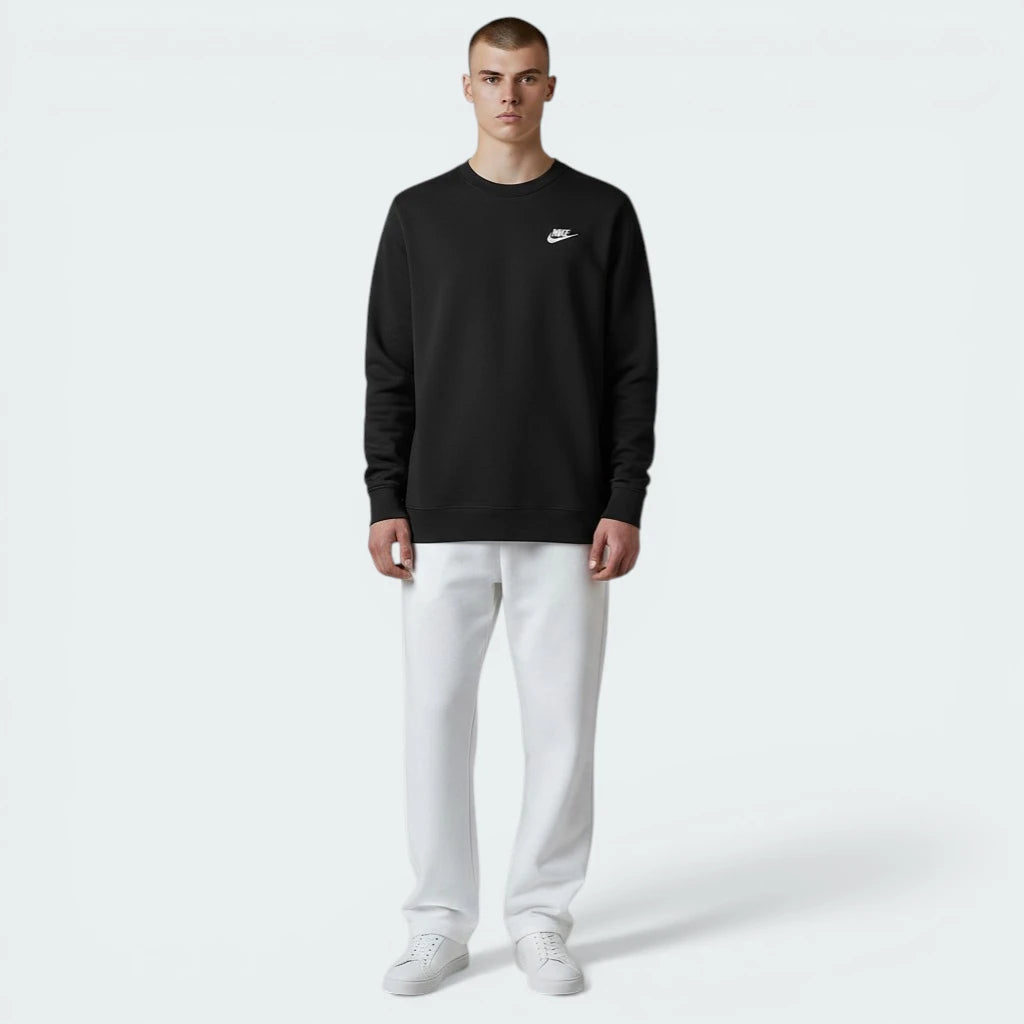 Person wearing a black long-sleeve shirt with a logo and white pants on a light gray background