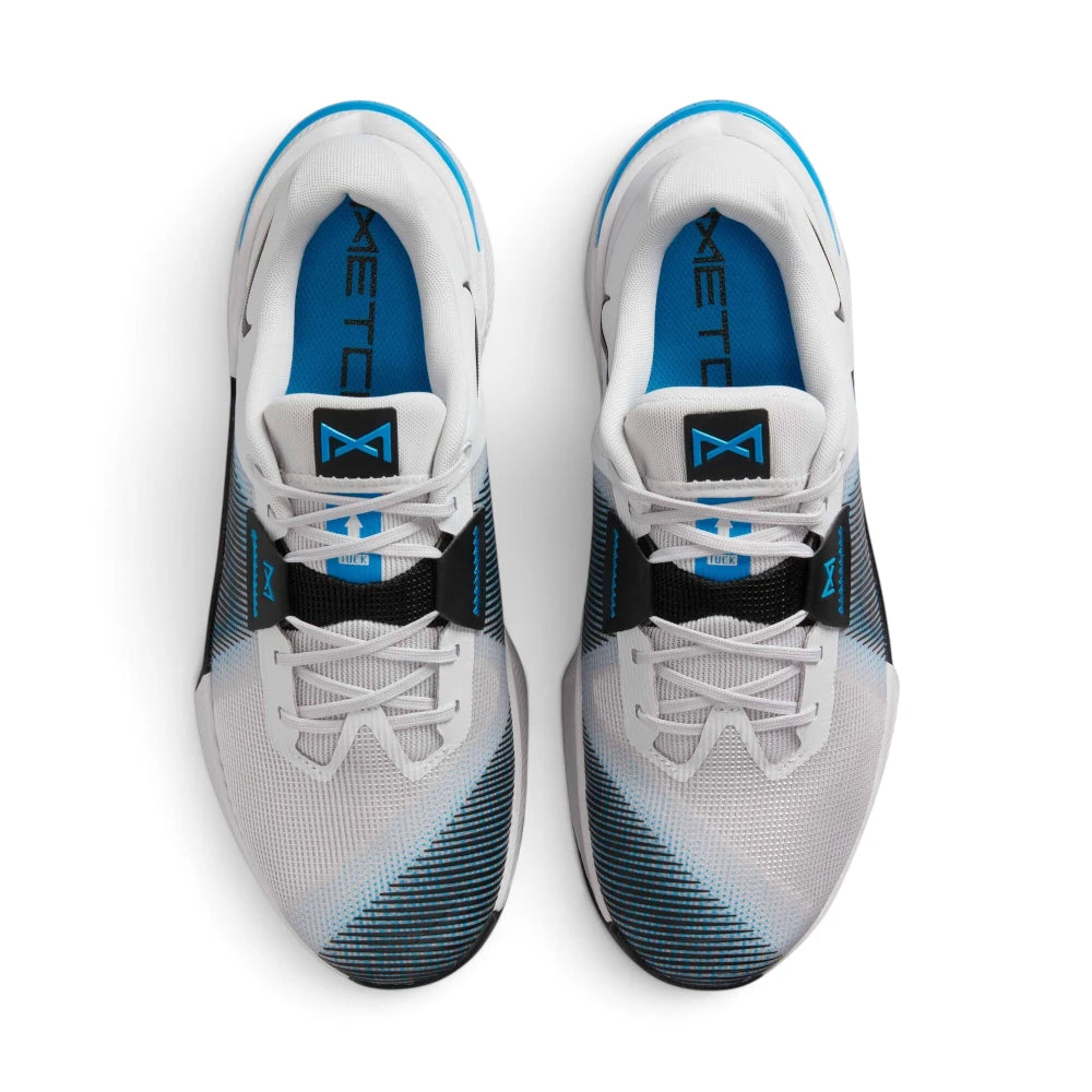 Aerial top-down view of both trainers, showing the grey mesh uppers, matching laces, blue cushioned insoles with Metcon branding, black lace bands, and blue tongue badge logos.