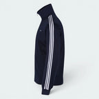 Focuses on the symmetry of the flat-laid track jacket, displaying the perfect alignment of the high stand-up collar, the white zip track, and the balance of the embroidered Trefoil logo.