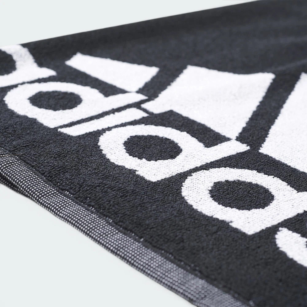 Details a close-up angle across the towel's surface, showing the dense, plush loop texture of the black cotton terry cloth and the precise definition where the white logo ink bonds to the fabric.