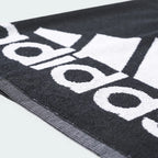 Details a close-up angle across the towel's surface, showing the dense, plush loop texture of the black cotton terry cloth and the precise definition where the white logo ink bonds to the fabric.