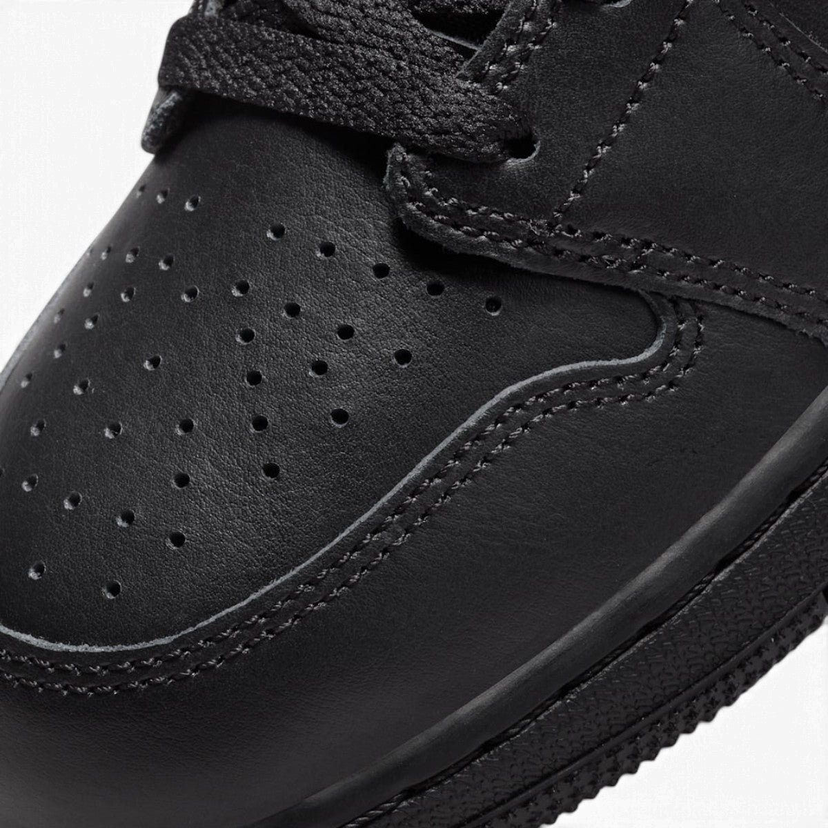Macro focus on the forefoot and eyestay, detailing the perforated toe box leather texture, tonal stitching, and flat black laces.
