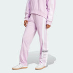 The Light Orchid Adibreak pants, highlighting the full-length white snap buttons and the contrast 3-Stripes against the soft purple base.