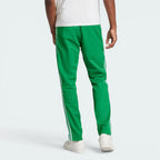 Green track pants with white stripes worn by a person on a white background
