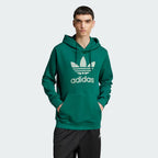 Model profile of the Collegiate Green Adidas hoodie, showcasing the relaxed regular fit and the structured ribbed cuffs.