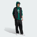 Person wearing a green hoodie, black vest, and black pants with white sneakers on a white background