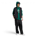 Person wearing a green hoodie, black vest, and black pants with white sneakers on a white background