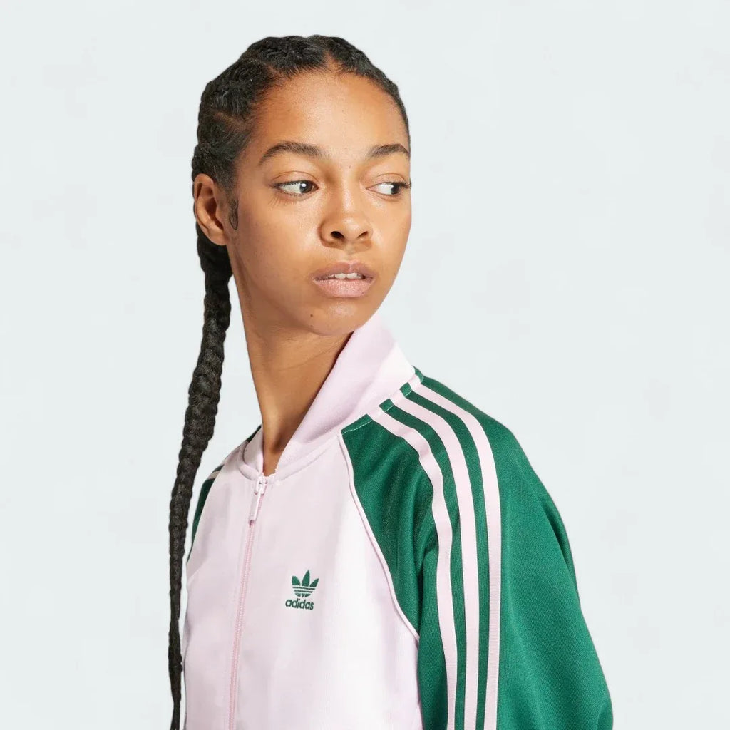 Close-up zoom on the fabric of the Adidas Adicolor Classics Loose Superstar Track Jacket in pink, showing the smooth interlock texture and the embroidered Trefoil logo detail on the chest.