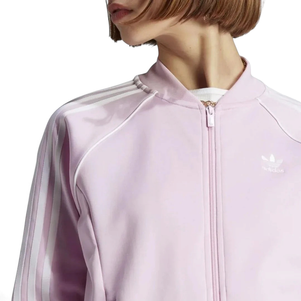 Close-up zoom on the fabric of the Adidas Adicolor Classics Superstar Track Jacket in pink, showing the soft texture and the embroidered Adidas Trefoil logo detail on the chest.
