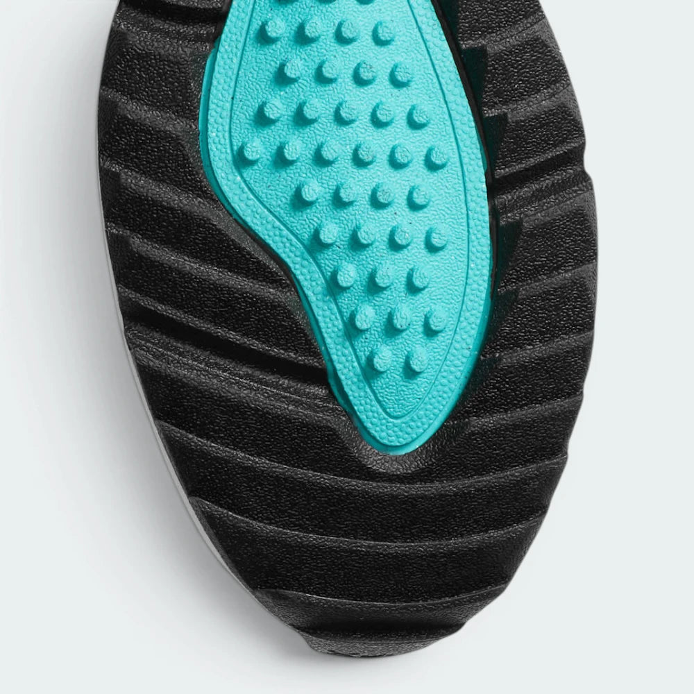 Close-up of a black textured shoe sole with a bright turquoise accent panel featuring raised circular studs, shown on a light gray background.
