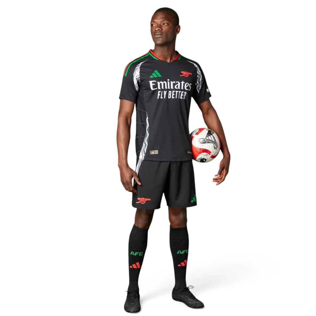 Full-length studio shot of a male model wearing the complete away kit, including the black authentic jersey, matching shorts with red accents, and black socks featuring team branding.