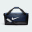 Highlights the Midnight Navy polyester body framed by black side panels and a black coated bottom base, featuring a bold white Nike Swoosh printed on the front, a zipped front storage pocket, and a black padded shoulder strap stamped with white "NIKE" block lettering.