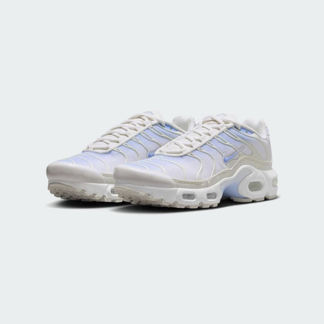 Angled view of two Nike Air Max Plus Juniors' Girls' trainers in psychic blue, white, and phantom, side by side, showcasing their bold design and layered construction.