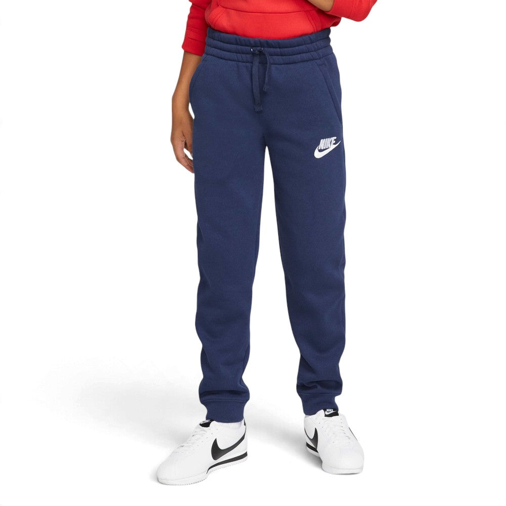Front-on view of a young model wearing the Midnight Navy fleece trousers paired with a red hoodie and white trainers, highlighting the tapered jogger silhouette.