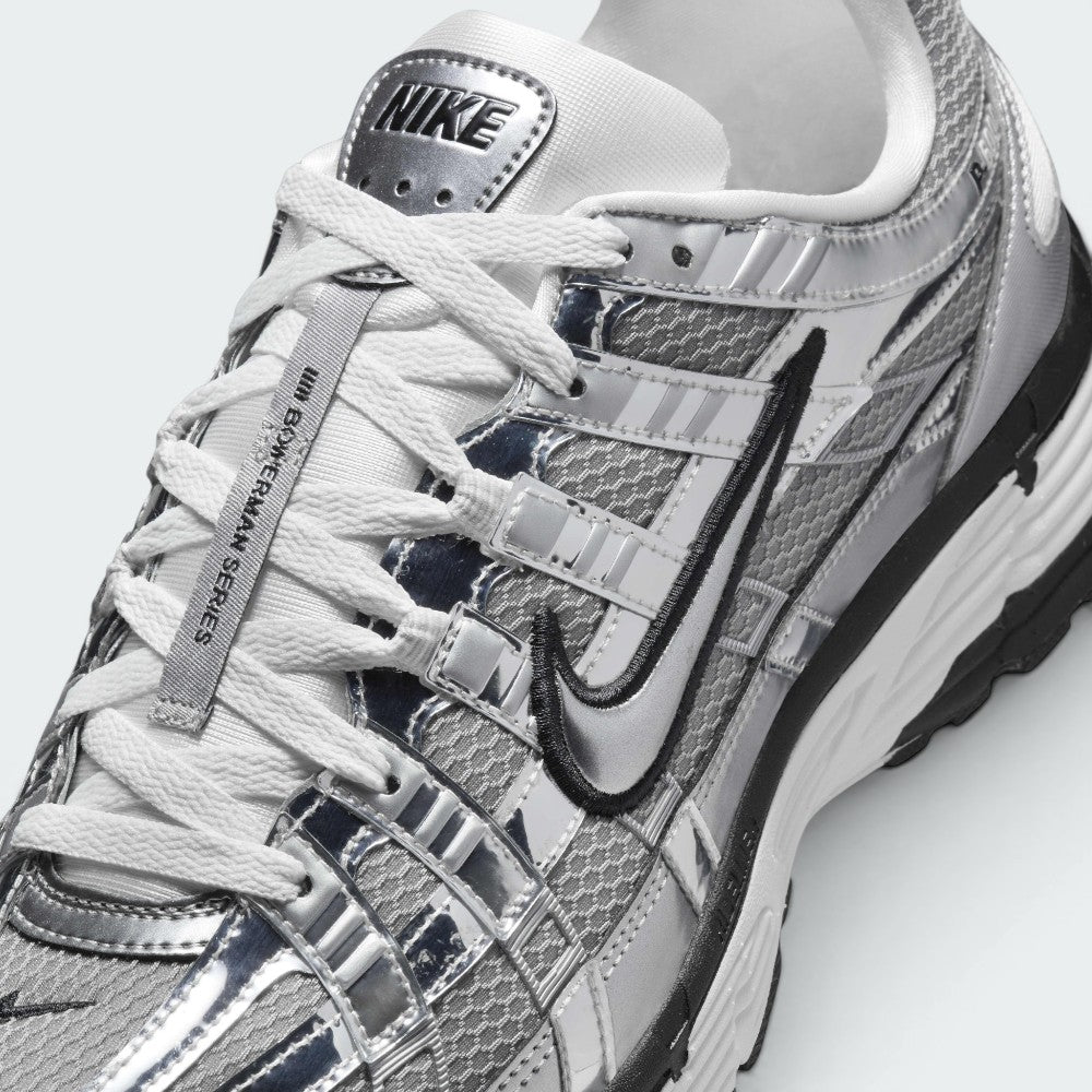 Details the micro-precision of the metallic mesh toe box, showing the chrome toe bumper, white laces, mini black Swoosh on the toe tip, and the silver "NIKE" tongue badge.