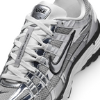 Details the micro-precision of the metallic mesh toe box, showing the chrome toe bumper, white laces, mini black Swoosh on the toe tip, and the silver "NIKE" tongue badge.