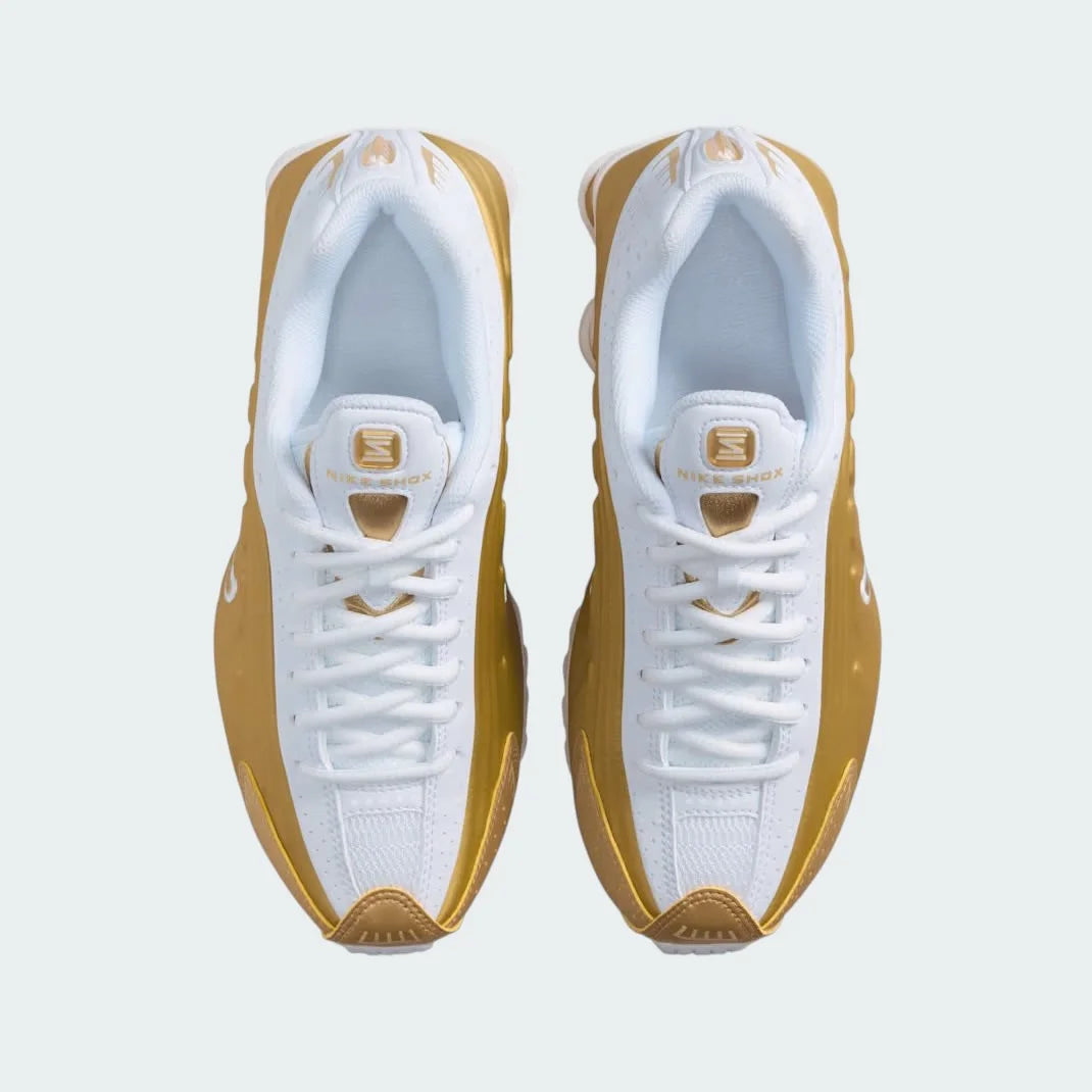 Top-down view of a pair of Nike Shox R4 Juniors' trainers in white and gold, highlighting their classic silhouette and lace-up closure.