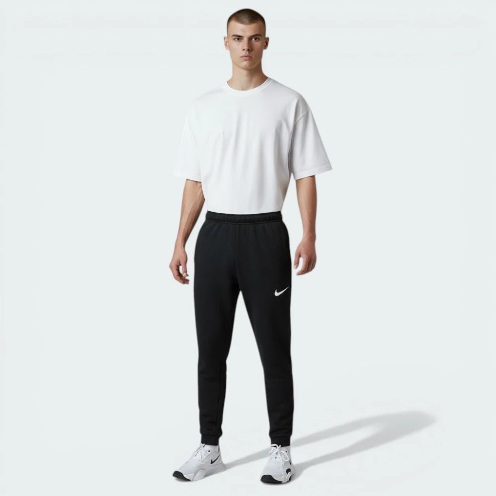 Front profile of the black Nike Dri-FIT taper trousers, showcasing the streamlined leg and the subtle white Swoosh on the left thigh.