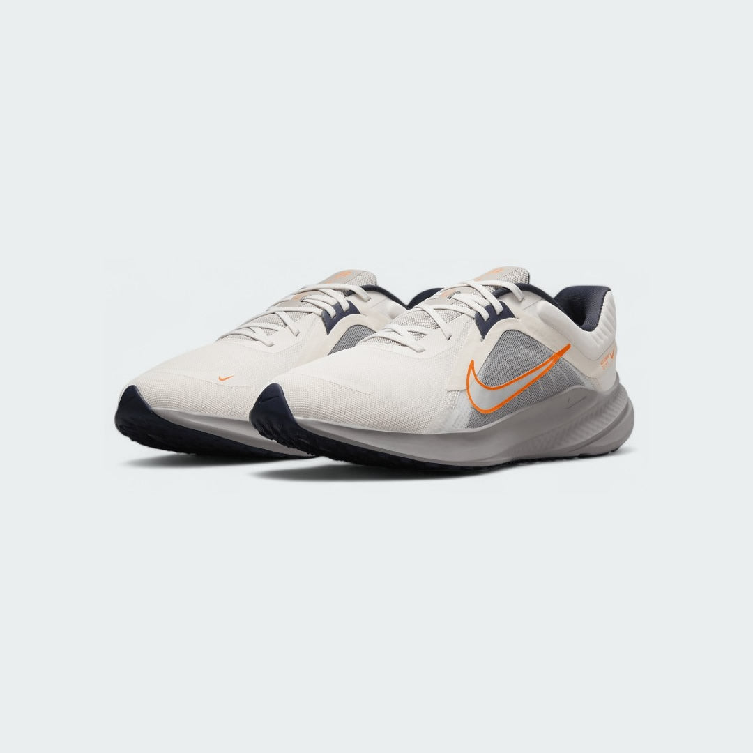 Angled view of two Nike Quest 5 Men's running shoes in sail with blue and orange accents, side by side, showcasing their lightweight design.