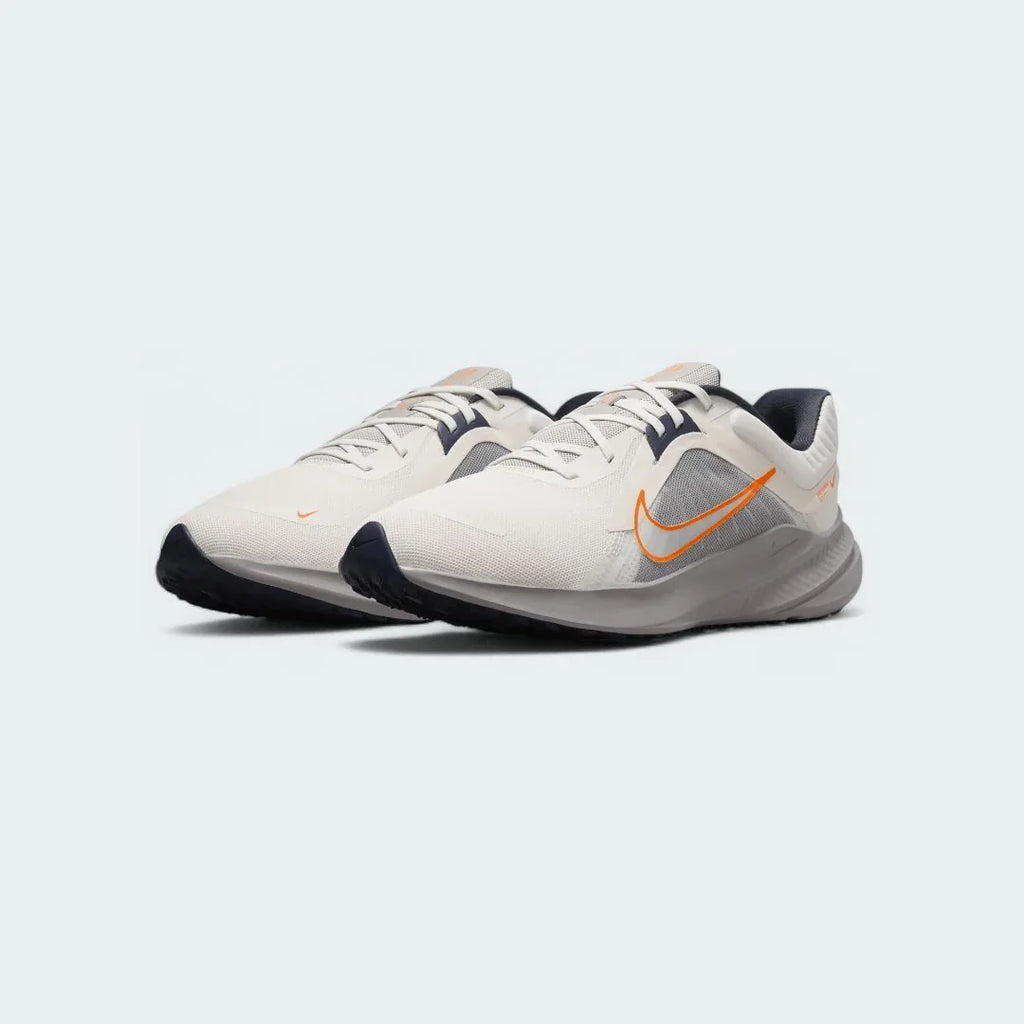 Angled view of two Nike Quest 5 Men's running shoes in sail with blue and orange accents, side by side, showcasing their lightweight design.