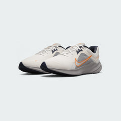 Angled view of two Nike Quest 5 Men's running shoes in sail with blue and orange accents, side by side, showcasing their lightweight design.