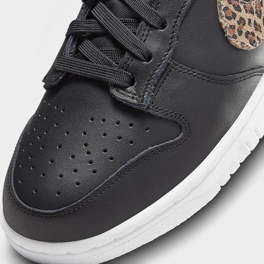 Close-up zoom on the front of the Nike Dunk Low SE Women's black leather trainers, showing the perforated toe box, lacing system, and textured leather upper.
