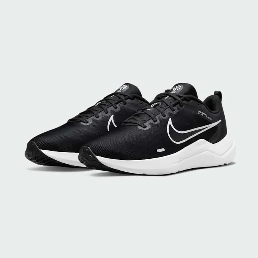 Angled view of two Nike Downshifter 12 Men's black and white training shoes, side by side, showcasing their versatile design and cushioned profile.