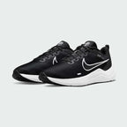 Angled view of two Nike Downshifter 12 Men's black and white training shoes, side by side, showcasing their versatile design and cushioned profile.