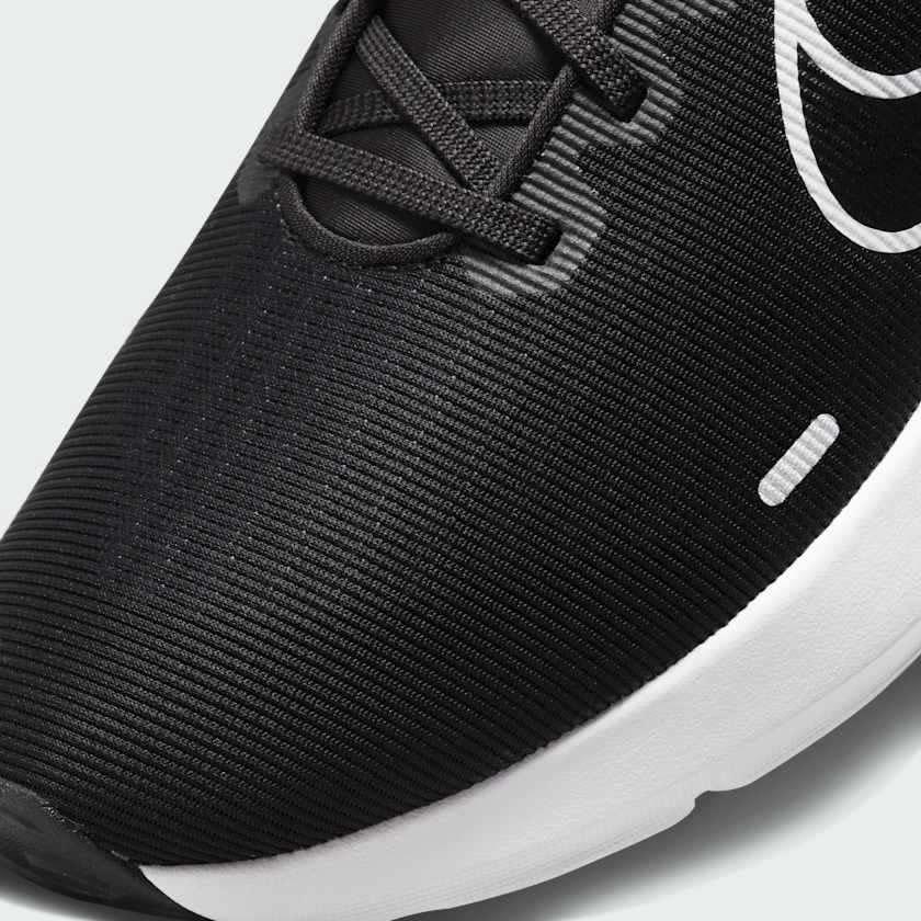 Close-up zoom on the front of the Nike Downshifter 12 Men's black training shoes, showing the mesh upper texture, lacing system, and supportive midfoot band.