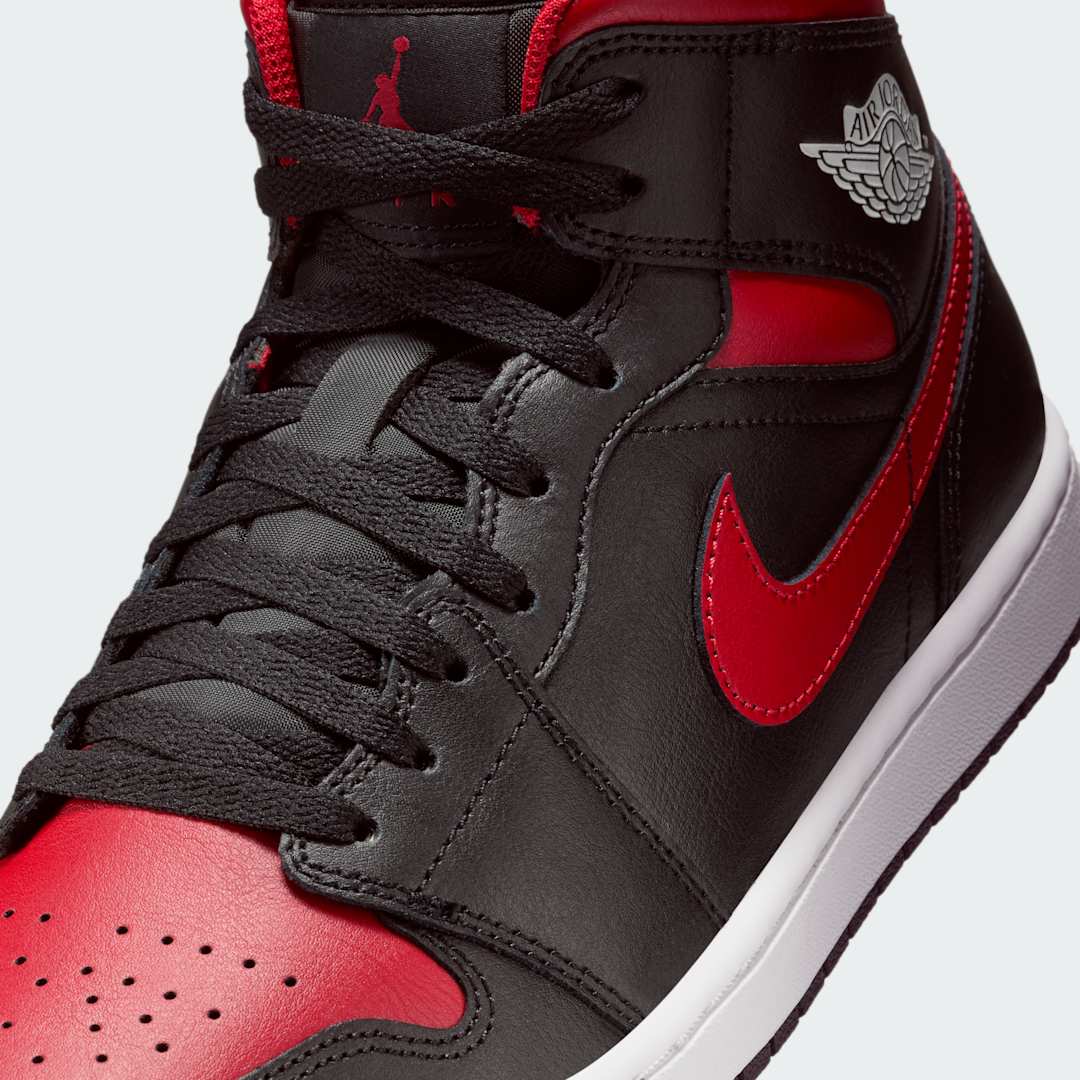 Close-up zoom on the front of the Air Jordan 1 Mid Men's black trainers, showing the perforated toe box, lacing system, and textured leather upper.