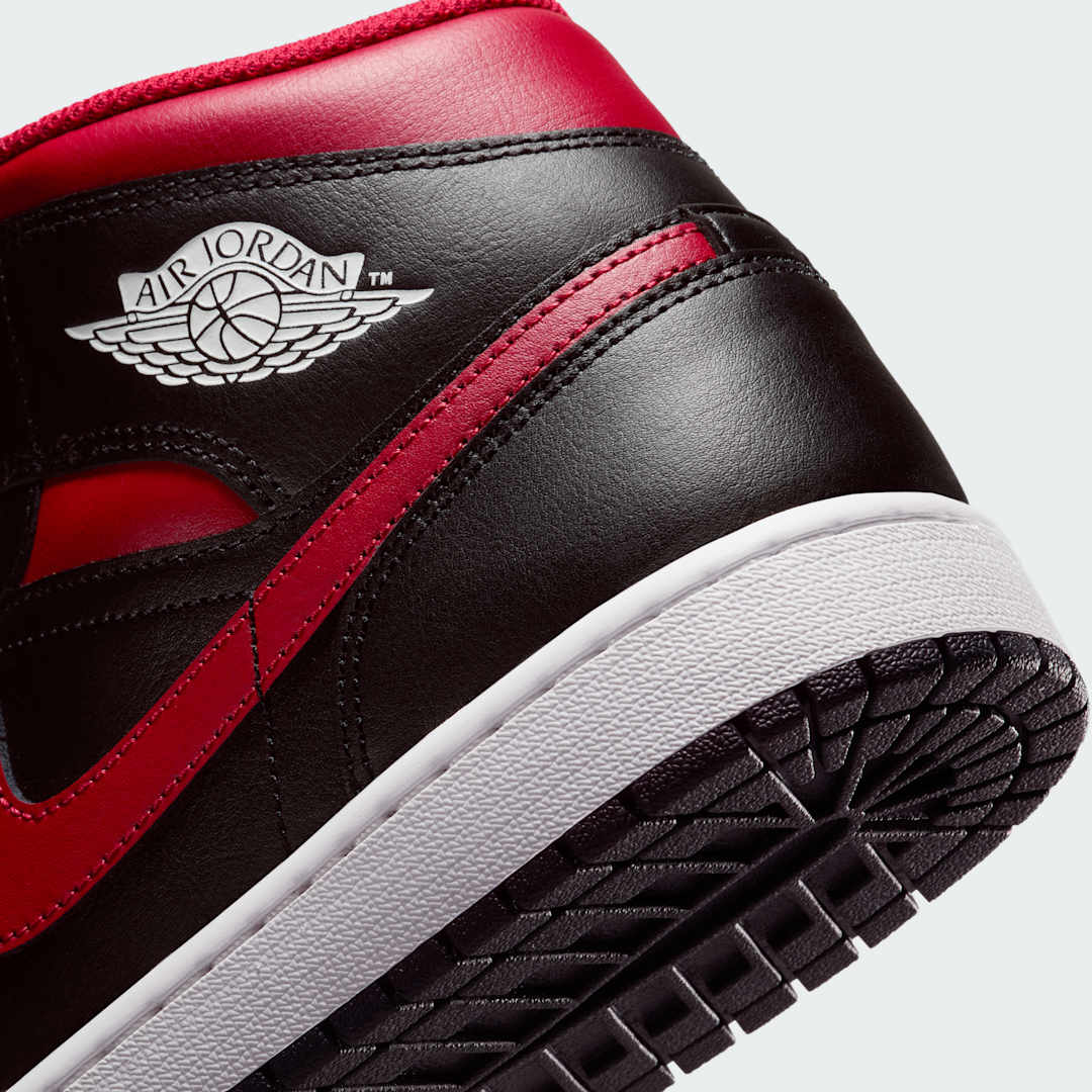 Detailed zoom on the side of the Air Jordan 1 Mid Men's trainers, highlighting the white midsole, red outsole, and black Nike Swoosh.