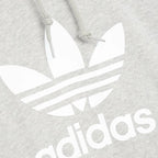 Close-up zoom on the Adidas Trefoil Hoodie Men's in grey heather, showing the soft French terry fabric texture and the embroidered (or printed) Trefoil logo detail.