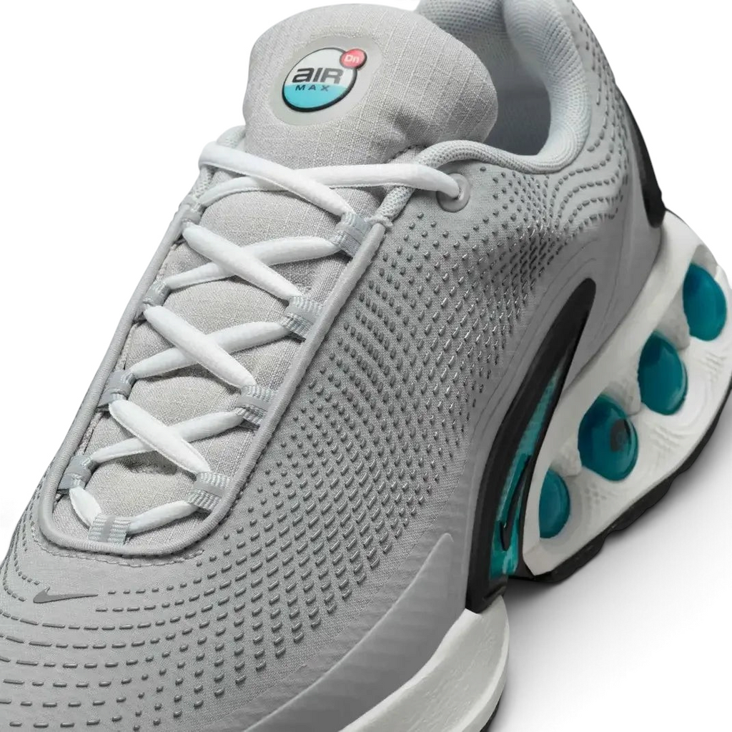 Close-up zoom on the front of the Nike Air Max DN Men's grey running shoes, showing the mesh upper texture, haptic print details, and lacing system.