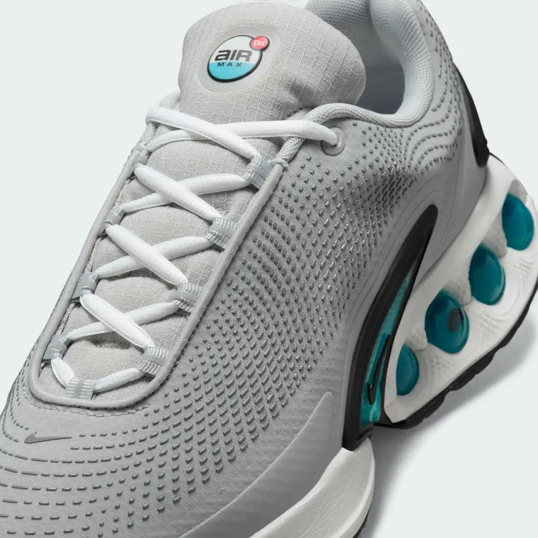 Close-up zoom on the front of the Nike Air Max DN Men's grey running shoes, showing the mesh upper texture, haptic print details, and lacing system.