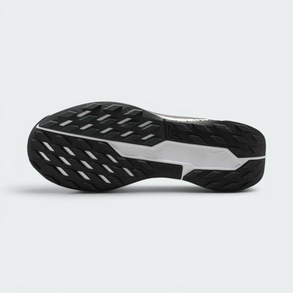 Displays the full-length black Nike Trail All-Terrain Compound (ATC) rubber sole, showcasing the multi-directional lug arrangement, flex grooves, and the central white stability shank stamped with "NIKE TRAIL" branding.
