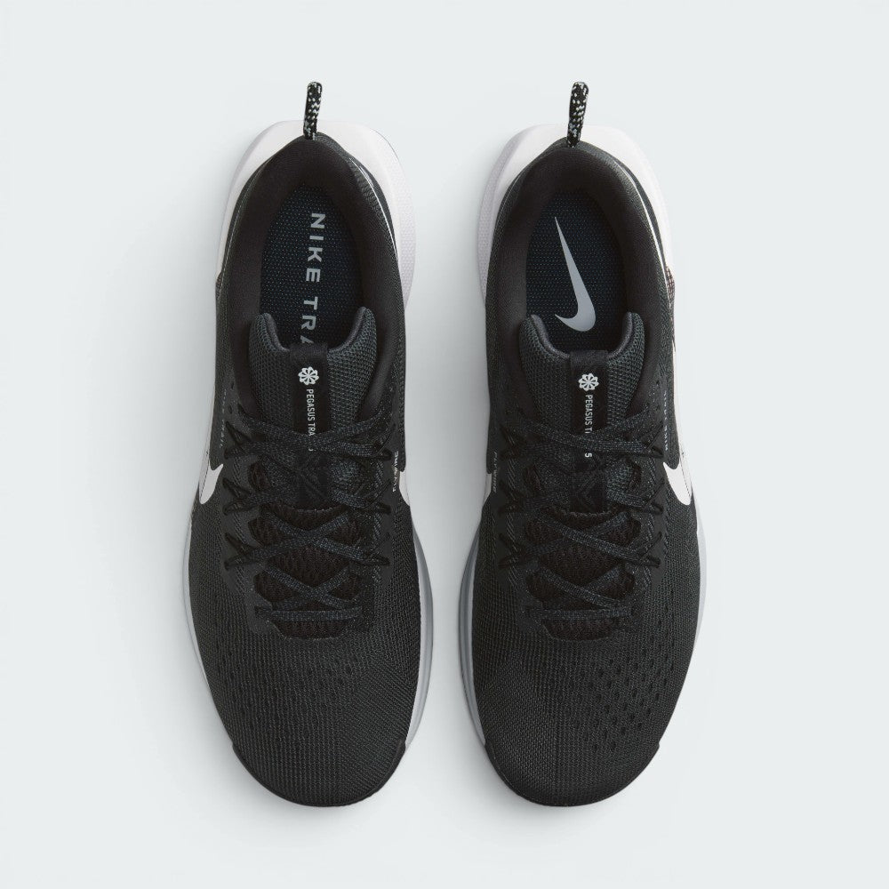 Focuses on the symmetrical lacing structure and top view of both shoes, displaying the black mesh tongues with "PEGASUS TRAIL 5" branding tags, black laces integrated with Flywire cables, and black insoles printed with white Nike trail logos.
