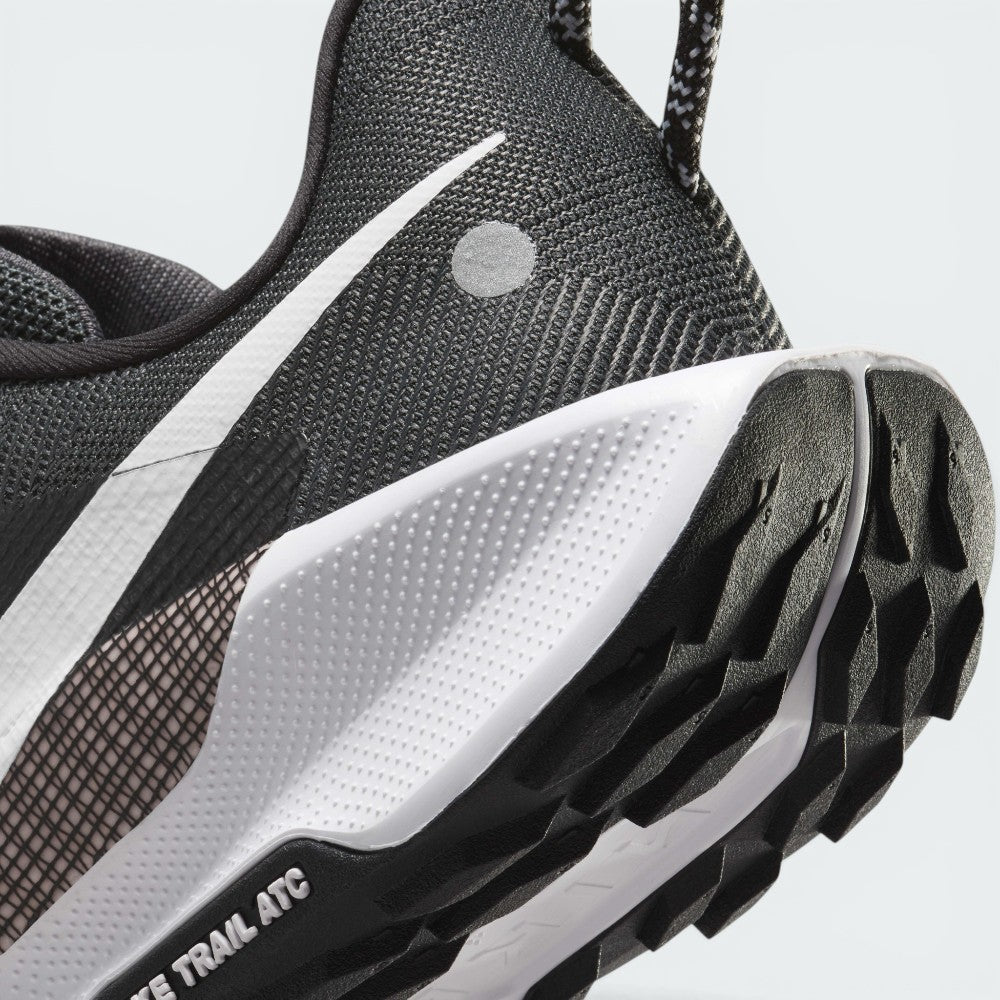 Detailed close-up of the rear lateral heel, showing the textured white ReactX foam heel clip, reflective circular accent dot on the black mesh counter, speckled pull tab, and the toothy black ATC rubber tread pods stamped with "NIKE TRAIL ATC".