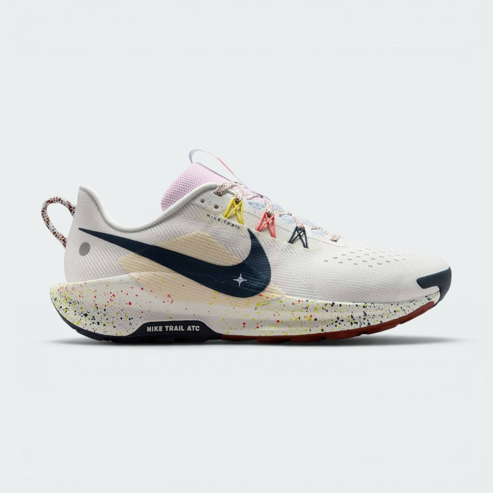 Highlights the lateral profile featuring an Armoury Navy Swoosh over a Summit White mesh upper, beige underlay grid panel, yellow and coral Flywire lace loops, paint-splattered ReactX foam midsole, and the "NIKE TRAIL ATC" outsole badge. Main image