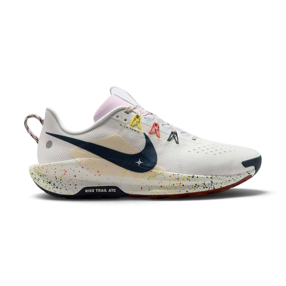Highlights the lateral profile featuring an Armoury Navy Swoosh over a Summit White mesh upper, beige underlay grid panel, yellow and coral Flywire lace loops, paint-splattered ReactX foam midsole, and the "NIKE TRAIL ATC" outsole badge. Main image