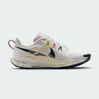 A Nike running shoe in a side profile view, featuring a white and light beige Flyknit upper with colorful speckles on the midsole, a black Swoosh, and multicolor laces.