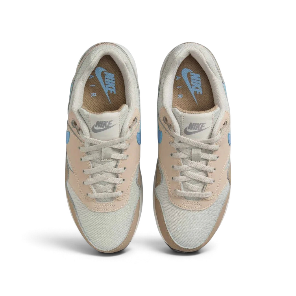 Top-down view of a pair of Nike Air Max 1 Juniors' trainers in light brown and blue, highlighting their classic silhouette and lace-up closure.